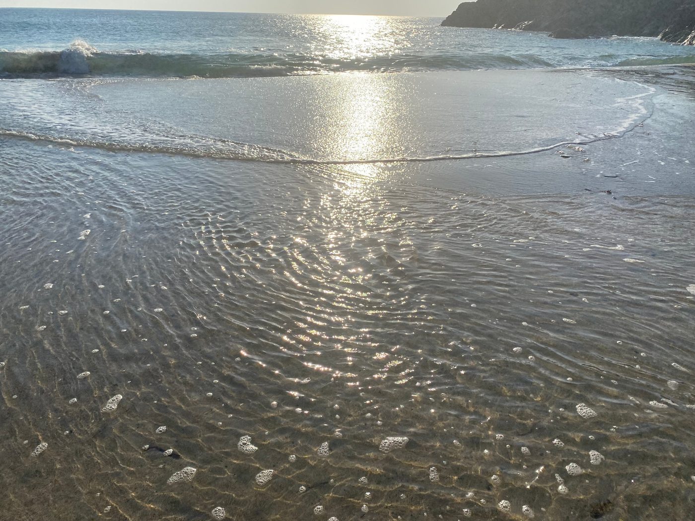 Sunlight reflecting across shallow seawater and ripple patterns on a sandy seabed