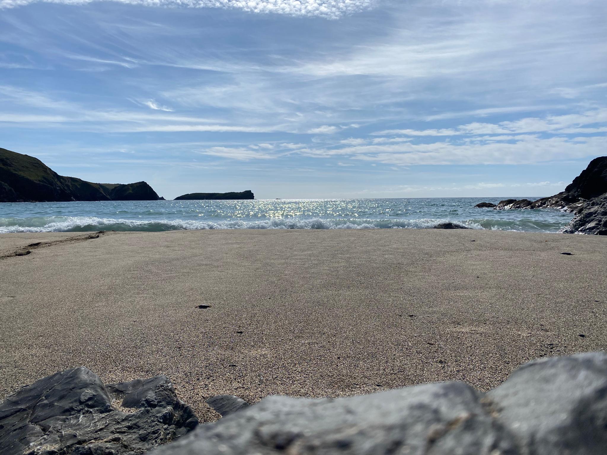 Wide ocean cove with pale sand, bright water and a blue sky streaked with thin clouds